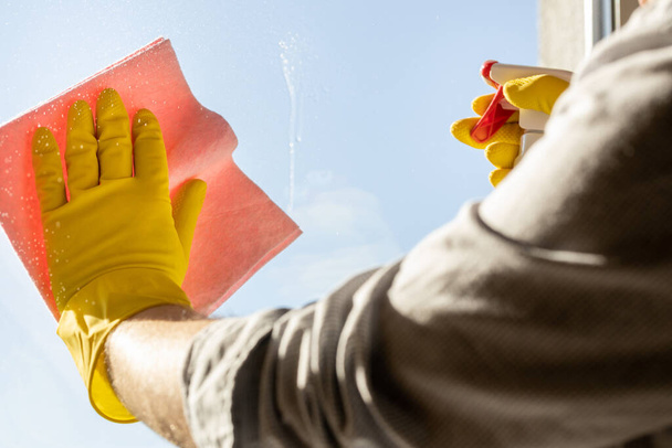 Современный мужчина моет окна дома, Офисная рубашка с завернутыми рукавами, розовая ткань, желтые резиновые перчатки, Концепция уборки дома также выполняется мужчинами  - Фото, изображение
