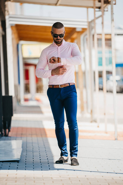 A cool handsome Caucasian man wearing an elegant light pink shirt and sunglasses posing outdoor - Zdjęcie, obraz