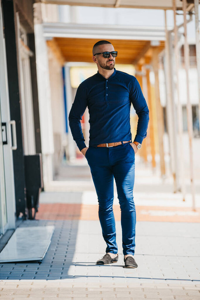 A cool handsome Caucasian man wearing an elegant blue shirt and sunglasses posing outdoor - Foto, imagen