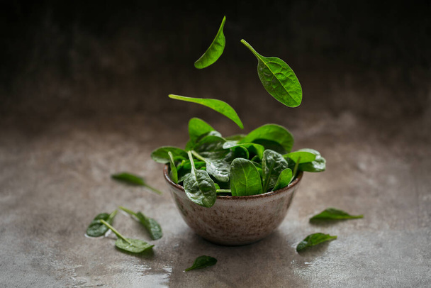 Leaves of fresh baby spinach in a Bowl. Flying leaves. Dark organic green leaves. Healthy vegan food lifestyle concept - Фото, зображення