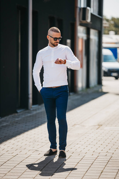 A cool handsome Caucasian man wearing an elegant white shirt and sunglasses posing outdoor - Foto, Imagen