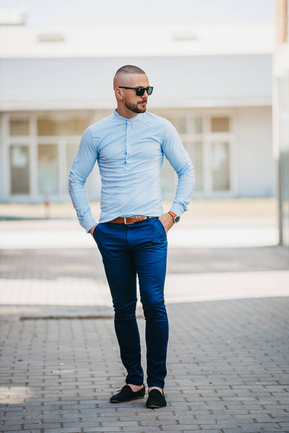 A cool handsome Caucasian man wearing an elegant lightblue shirt and sunglasses posing outdoor - Photo, Image
