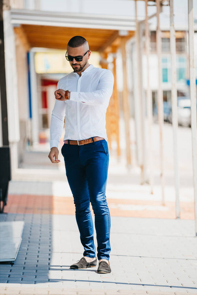 A cool handsome Caucasian man wearing an elegant white shirt and sunglasses posing outdoor - Foto, Imagem