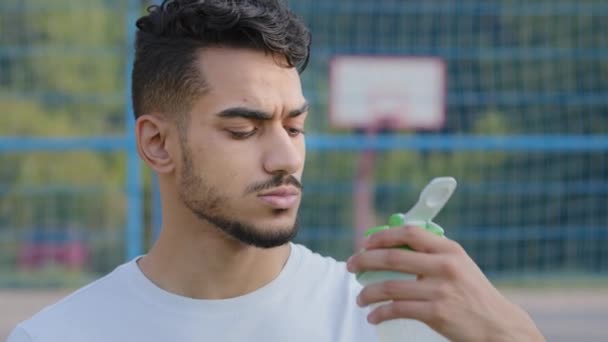 Closeup of middle eastern indian man athlete latino runner quenching thirst after jogging. Young arab guy drinks clean fresh water from sports bottle during daily training at city summer stadium - Footage, Video