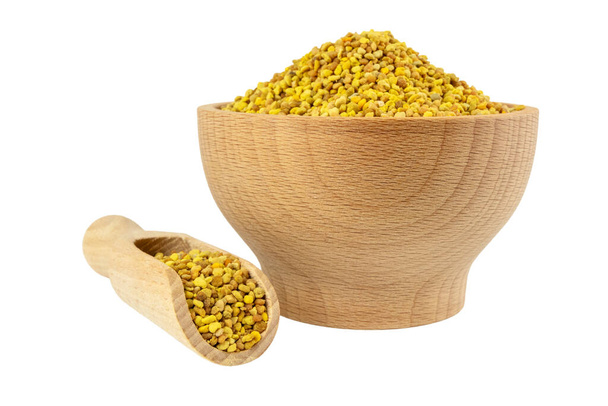 Bee pollen in wooden bowl and scoop isolated on white background. Natural herbal medicine to relieve inflammation, influenza, boosts liver health, strengthens immune system, reduces stress and used as a dietary supplement. - Photo, Image