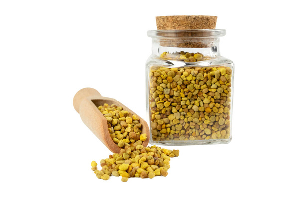 Bee pollen in wooden scoop and glass jar on isolated on white background.Natural herbal medicine to relieve inflammation, influenza, boosts liver health, strengthens immune system, reduces stress and used as a dietary supplement. - Photo, Image