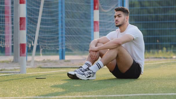 真剣に、試合やトレーニングセッションの後に休憩し、ゴールに対してサッカー場の芝生の上に座って中東のサッカー選手を放送。夏のスポーツウェアの千年運動選手は試合開始を待っています - 映像、動画