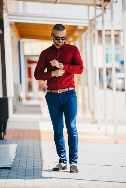 A cool handsome Caucasaian man wearing an elegant red shirt and sunglasses posing outdoor - Fotoğraf, Görsel