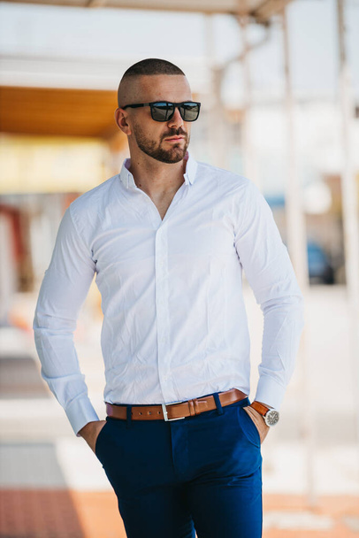 A cool handsome Caucasian man wearing an elegant white shirt and sunglasses posing outdoor - Fotoğraf, Görsel