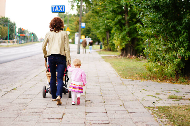 POZNAN, POLAND - Sep 10, 2013: A woman walking with her child and baby with stroller at a sidewalk - 写真・画像