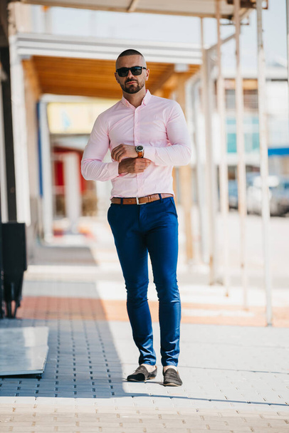 A cool handsome Caucasian man wearing an elegant light pink shirt and sunglasses posing outdoor - Foto, imagen