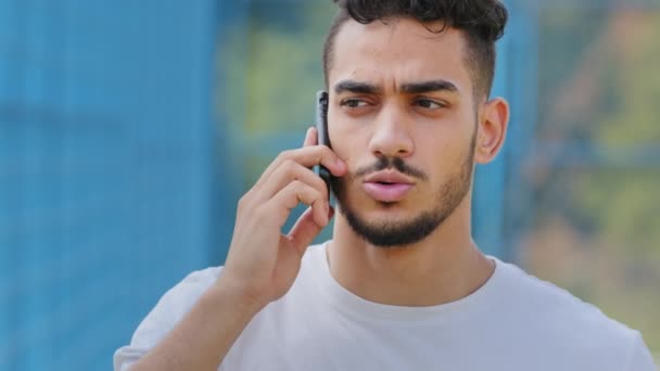 Młody, poważnie zaniepokojony arabski student, mężczyzna atleta w letniej odzieży sportowej, trzymający smartfona, Indianin rozmawiający przez nowoczesny telefon komórkowy, raportujący złe wieści, ma nieprzyjemną rozmowę - Materiał filmowy, wideo
