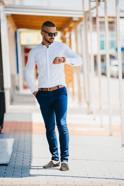 A cool handsome Caucasian man wearing an elegant white shirt and sunglasses posing outdoor - Photo, Image