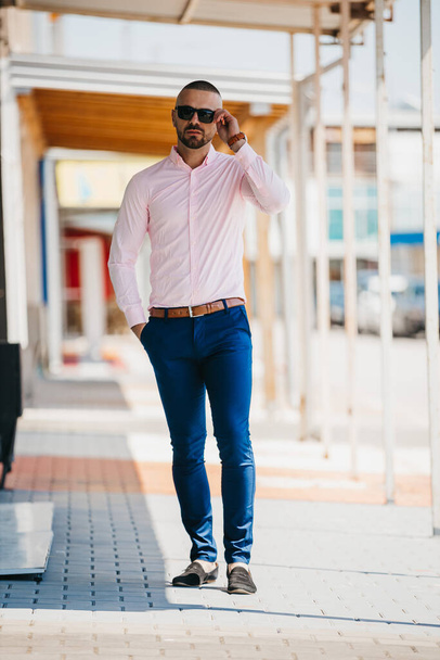 A cool handsome Caucasian man wearing an elegant light pink shirt and sunglasses posing outdoor - Foto, imagen