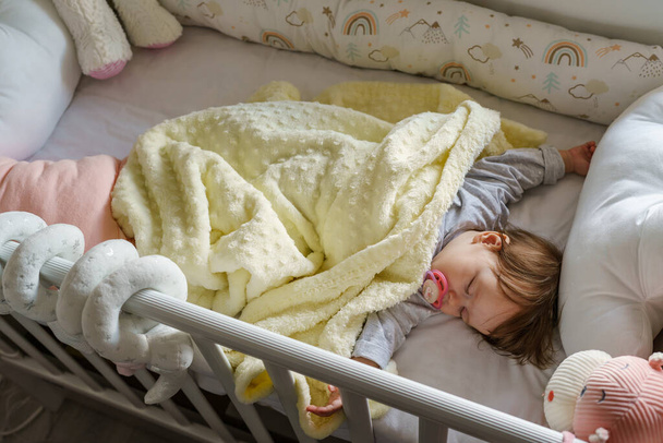 Вид сверху на маленькую младенческую девочку, лежащую в сумасшедшей кровати дома во сне - детская паранойя и концепция взросления - Фото, изображение