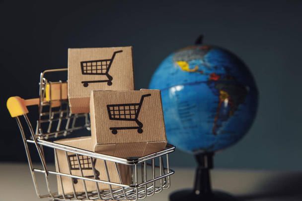 Globe en supermarkt winkelwagentje met dozen. Wereldwijd verkoop- en internetverkoopconcept - Foto, afbeelding