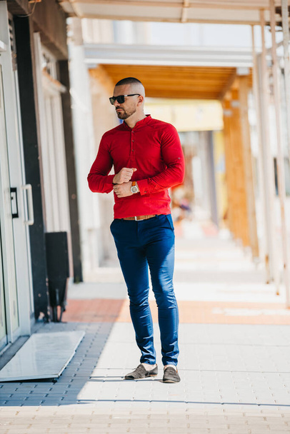 A cool handsome Caucasian man wearing an elegant red shirt and sunglasses posing outdoor - Photo, Image