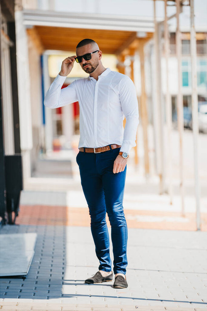 A cool handsome Caucasian man wearing an elegant white shirt and sunglasses posing outdoor - Φωτογραφία, εικόνα