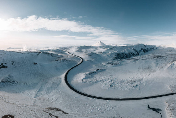 aerial drone view Uphill road landscape in winter at Iceland. Asphalt road with sideways full of snow during winter with blue sky. Photo taken in Iceland. - Φωτογραφία, εικόνα