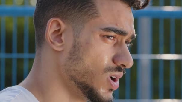 A fáradt, izzadt arab spanyol fickó a stadionban futás után törli le az izzadságot a homlokáról. Komolyan koncentrált férfi arc. Millenniumi férfi sportoló bajnok nyáron sportruházat végzett fárasztó fárasztó edzés - Felvétel, videó