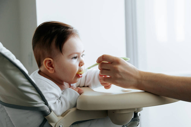 Portrait of a sweet child, who is fed baby food from a spoon - Foto, afbeelding