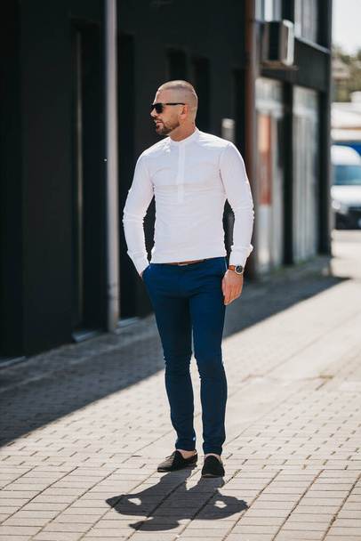 A cool handsome Caucasian man wearing an elegant white shirt and sunglasses posing outdoor - Foto, Bild