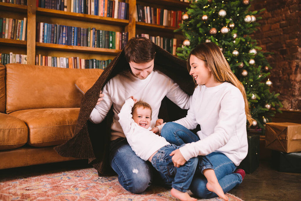Magische kerstsfeer in gezellig huis. Jonge familie met kind geniet van spelen op de vloer bedekt met deken in de buurt van kerstboom op nieuwjaarsvakantie. Gelukkige jeugd. Vakantie winteravond thuis. - Foto, afbeelding