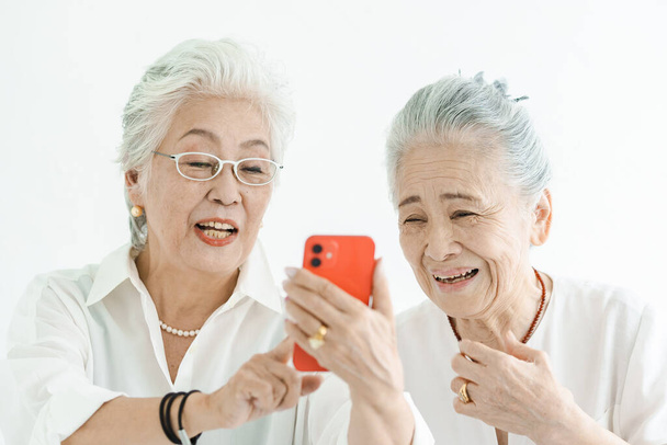 Las mujeres mayores mirando las pantallas de teléfonos inteligentes con una sonrisa  - Foto, Imagen