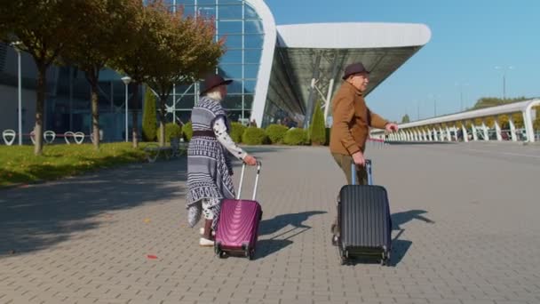 Happy grandmother grandfather walking with luggage suitcase bags to airport hall, celebrate dancing - Footage, Video