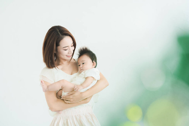 Asiática mamá sosteniendo un bebé en el brillante habitación - Foto, Imagen