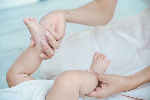Руки матери поддерживают ноги ребенка в комнате - Фото, изображение
