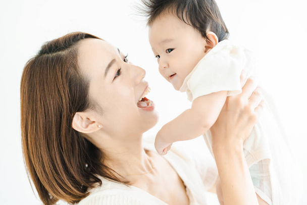 Азиатская мама держит ребенка в светлой комнате - Фото, изображение