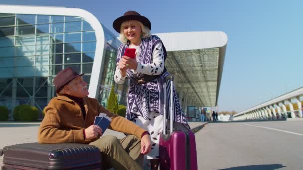 Senior nyugdíjas turisták nagymama nagyapa vesz jegyeket online mobiltelefonon repülőtér közelében - Felvétel, videó