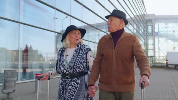 Mayores marido esposa jubilados turistas van a la terminal del aeropuerto para abordar con el equipaje sobre ruedas - Metraje, vídeo