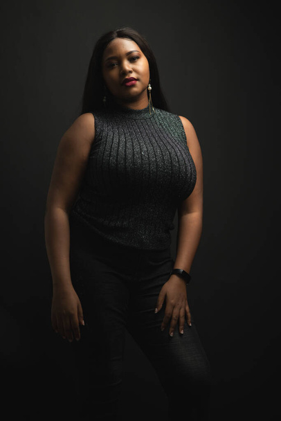 Portrait of black woman plus size posing and smiling with confident while looking toward to camera in the dark background. - Foto, afbeelding