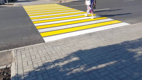 zwei Fußgänger, die die Straße überqueren, auf einer neuen gelb-weißen Markierung eines Fußgängerüberwegs, Lebenssicherheit, Verkehrskonzept. - Foto, Bild