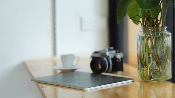 Layout plano de um computador tablet digital portátil na mesa com câmera retro, xícara de café e planta interior no fundo - Foto, Imagem
