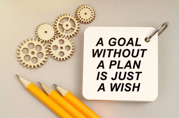 Business and finance concept. On the table are gears, pencils and a notebook with the inscription - A Goal Without a Plan Is Just a Wish - Foto, Imagen
