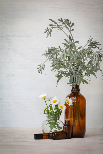 白い背景に琥珀のエッセンシャルオイルボトルとディスプレイ菊の花。 - 写真・画像