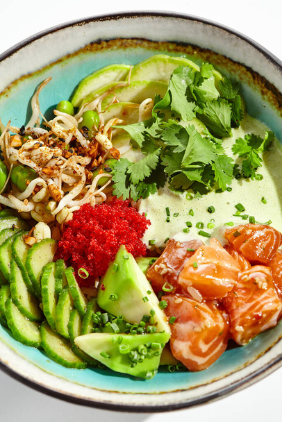 Healthy food - poke bowl with salmon, rice, cucumber, avocado, edamame beans, soybean sprouts and ponzu sauce. Hawaiian meal poke bowl with salmon isolated on white background - Foto, Bild