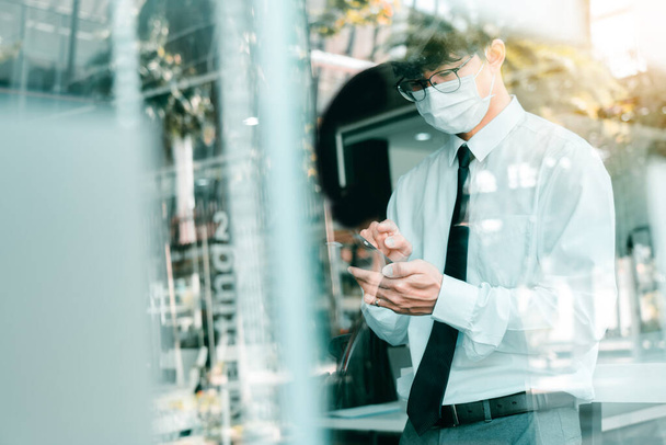 Pracownicy stojący w pracy, korzystający z telefonów i noszący maski podczas epidemii wirusa. - Zdjęcie, obraz