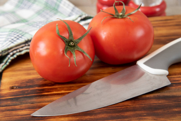 Rijp rode tomaten op een houten snijplank met een keukenmes - Foto, afbeelding
