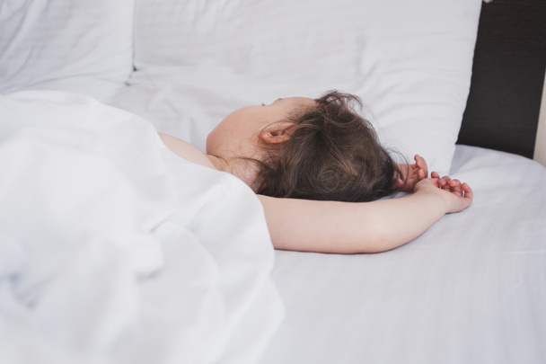 Το παιδί κοιμάται γλυκά στο κρεβάτι. Κοιμισμένα παιδιά στο κρεβάτι των γονιών. Το παιδί κοιμάται ήσυχα σε λευκά σεντόνια.. - Φωτογραφία, εικόνα