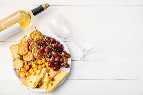 Bandeja con galletas crujientes y queso y botella de vino sobre fondo de madera blanca - Foto, Imagen