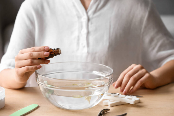 Maestro de la manicura añadiendo aceite esencial al agua en un tazón en la mesa - Foto, imagen