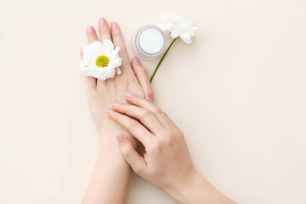 Mains féminines avec pot de crème cosmétique et fleurs de camomille sur fond clair - Photo, image