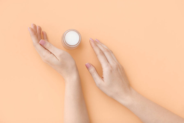 Female hands with jar of cosmetic cream on color background - 写真・画像