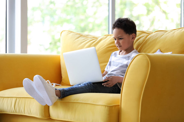 Pequeño chico afroamericano con portátil viendo dibujos animados en el sofá en casa - Foto, imagen