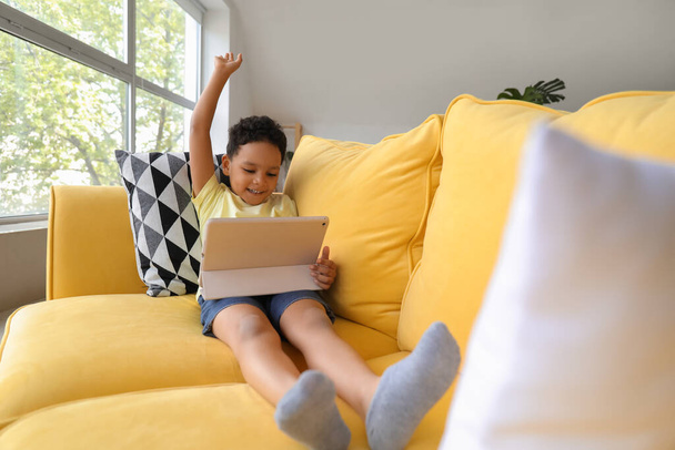 Tablet bilgisayarlı küçük Afro-Amerikalı çocuk evdeki kanepede çizgi film izliyor. - Fotoğraf, Görsel