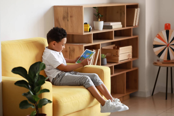 Little African-American boy with tablet computer watching cartoons on armchair at home - Foto, imagen